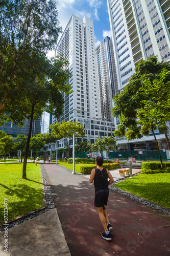 Bonifacio Global City, Taguig, Metro Manila - Aug 2020: A man jogs at a park in the middle of the city. Morning scene in Fort Bonifacio. Back shot, wide angle. photo