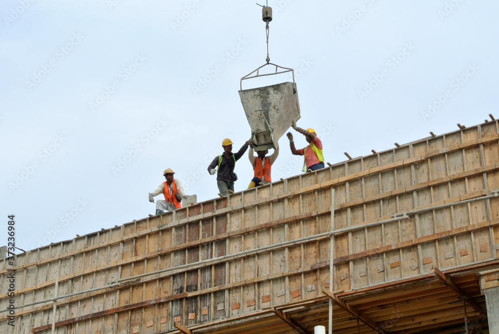 Naklejka premium JOHOR, MALAYSIA -MAY 06, 2016: A group of construction workers pouring concrete using concrete bucket into the column formwork at the construction site. 