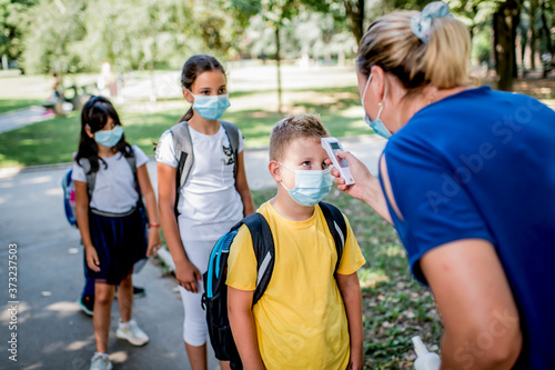 Female teacher using thermometer temperature screening on children for fever against the spread virus while student is coming back to school.