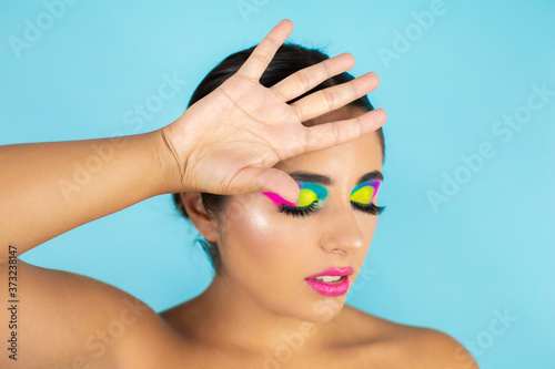 Beauty portrait of female model with vivid makeup on blue background.