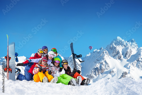 Large group of happy young adults lay in snow wave hands with snowboards and ski over mountain peaks