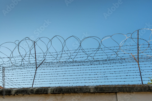 Barbed wired fence on jail wall against perfect blue sky with copy space.