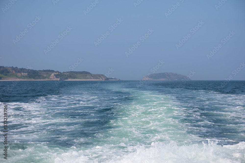 Wake from a motorboat sailing along the menai strait at anglesey. Puffin island and the coast with blue sea and a summer sky.