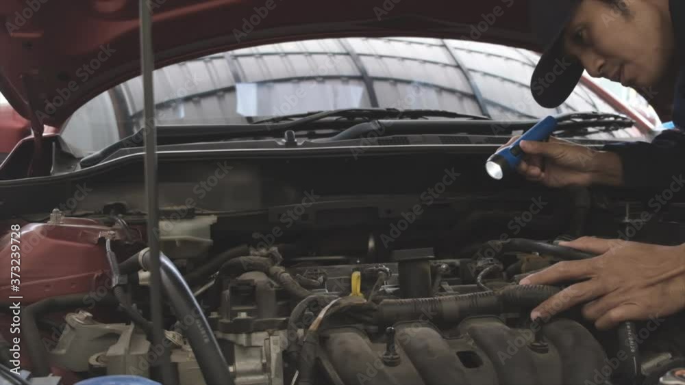 Asian Man mechanic inspection Shine a torch car engine checking bug in engine from application smartphone.Red car for service maintenance insurance with car engine.for transport automobile automotive