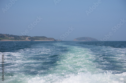 Wake from a motorboat sailing along the menai strait at anglesey. Puffin island and the coast with blue sea and a summer sky.