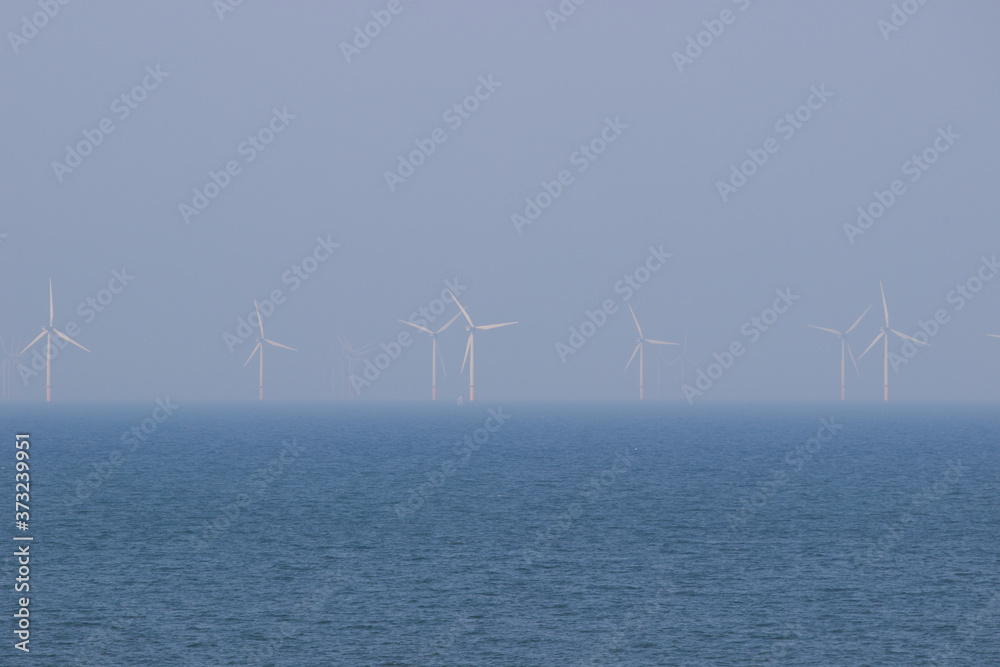 Off shore wind farm producing clean, renewable energy at Colwyn bay, North Wales. Wind turbines against a blue sky.