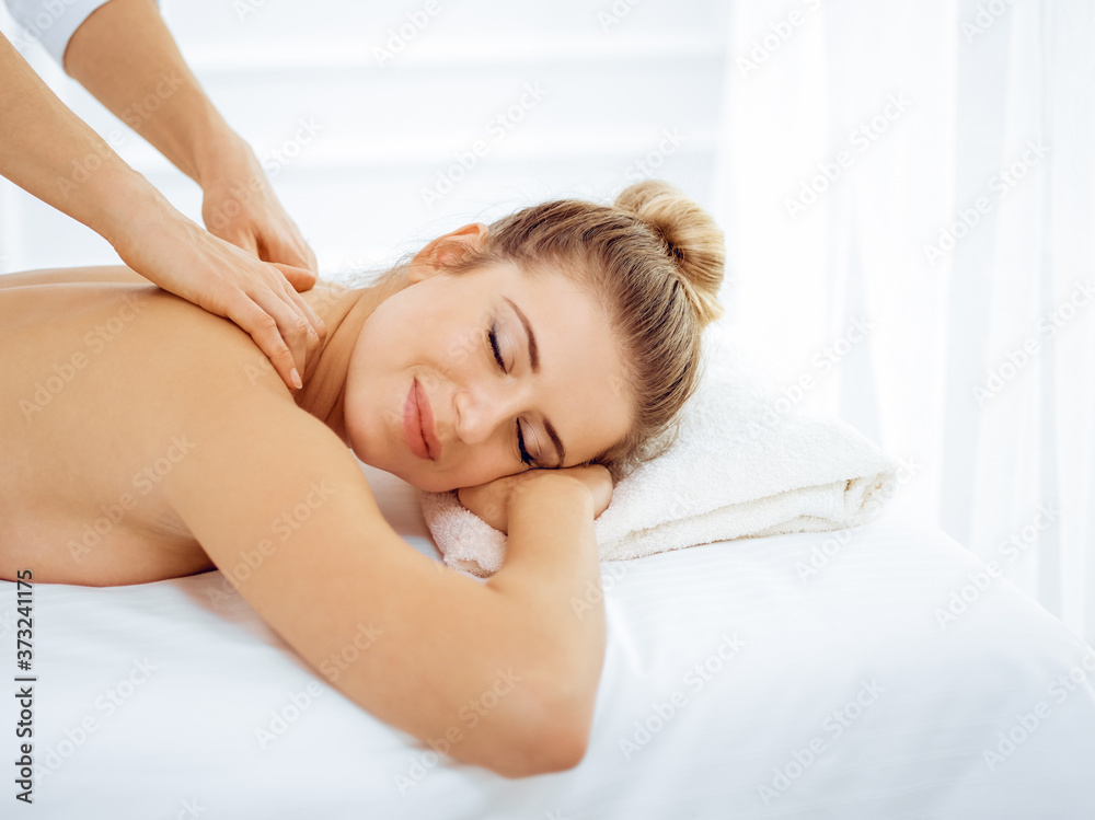 Young and blonde woman enjoying massage of back in spa salon. Beauty concept Young and blonde woman enjoying massage of back in spa salon. Beauty concept