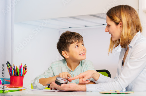 Autistic boy during ABA therapy look at teacher pointing to lesson timer learning to learn class procedures and understanding time concept