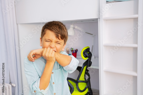 Close portrait of little autistic boy bite hands with strong negative face expression
