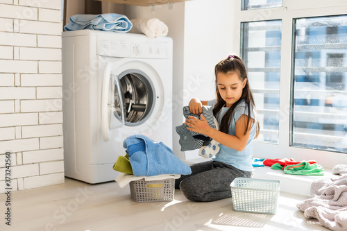 Beautiful child girl little helper is having fun and playing while doing laundry at home.
