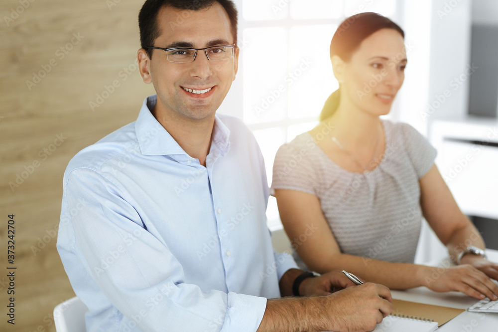 Businessman and hispanic business woman working with computer in sunny office. Group of diverse people