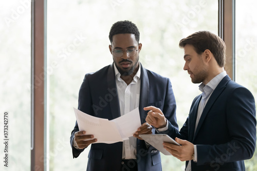 Serious caucasian businessman consulting african colleague about contract details, attentive consultant explaining black customer document positions, multiethnic manager and client discussing deal