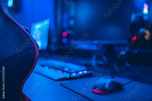 Professional cyber video gamer studio room with personal computer armchair, keyboard for stream in neon color blur background. Soft focus