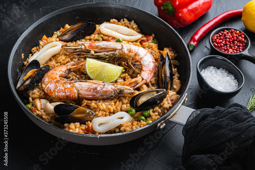 Paella traditional spanish dish served in frying pan, on black textured surface