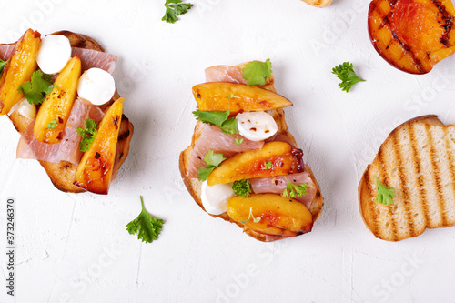 Bruschetta with grilled peaches, prosciutto and mozzarella topped with parsley and cilantro served on the white table. Top view photo