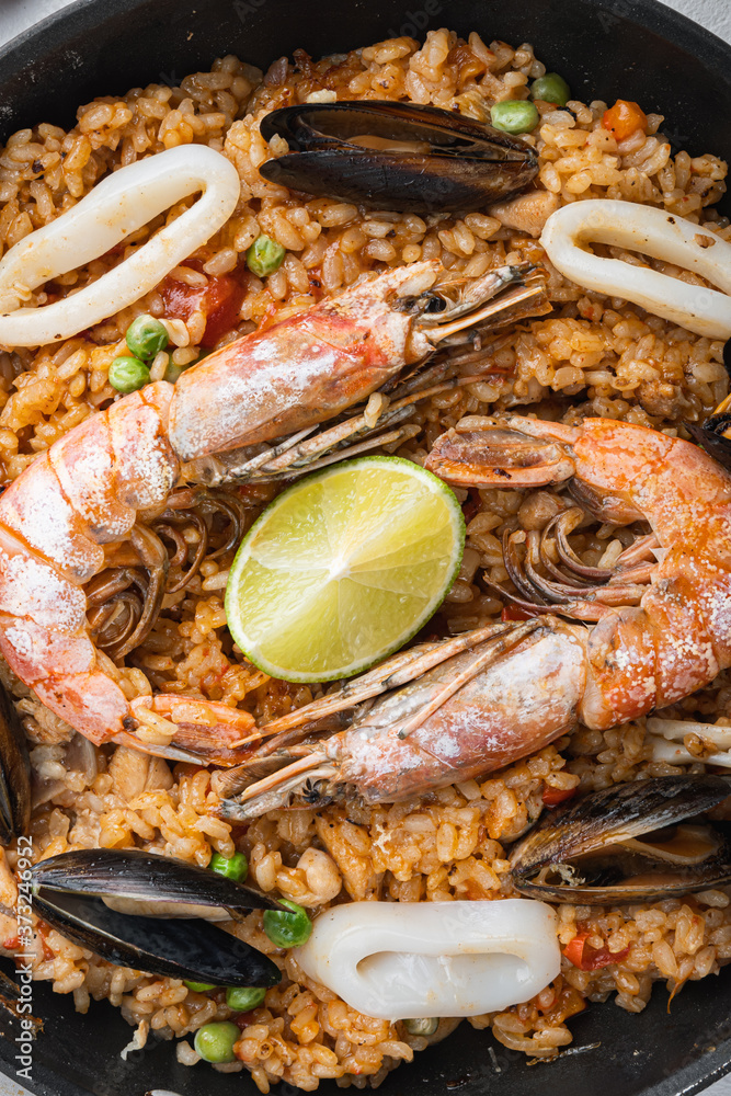 Seafood and chicken paella with rice, mussles, shrimps,chicken, tomatoes and wine in pan on white textured background, flat lay
