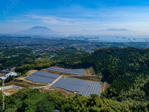 遠景の桜島を背景に空撮されたソーラーパネルのある風景が美しい。