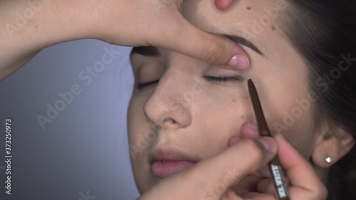 Process of Professional Makeup for beautiful and gorgeous woman sitting at the Studio. Make up Artist applying eyeliner to the upper eyelid of a brown-eyed girl