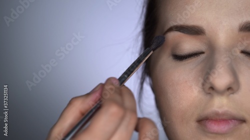 Close up of process of Professional Makeup for beautiful and gorgeous woman sitting at the Studio. Make up Artist applies blush with brush on eyelid