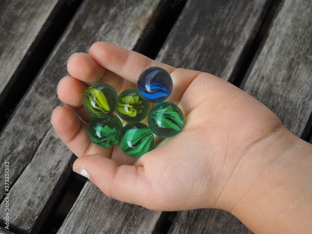 Colorful glass balls in the hand of a small child with an old wooden table in background