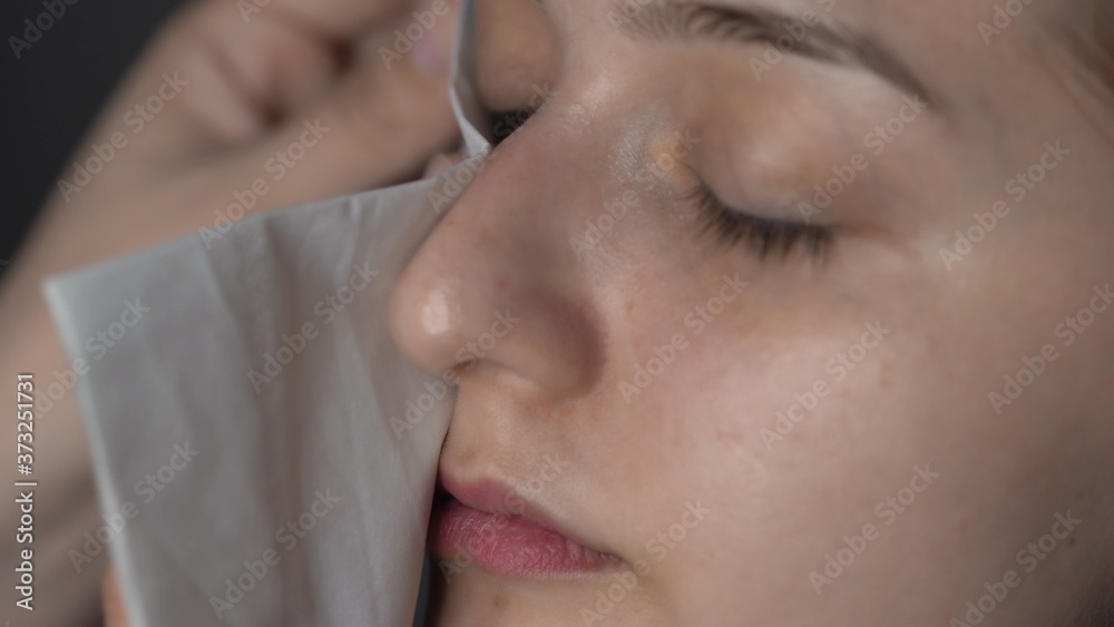 Close up of make-up artist making professional make-up for young woman in beauty studio. Makeup Artist uses paper wipe to clean model's face