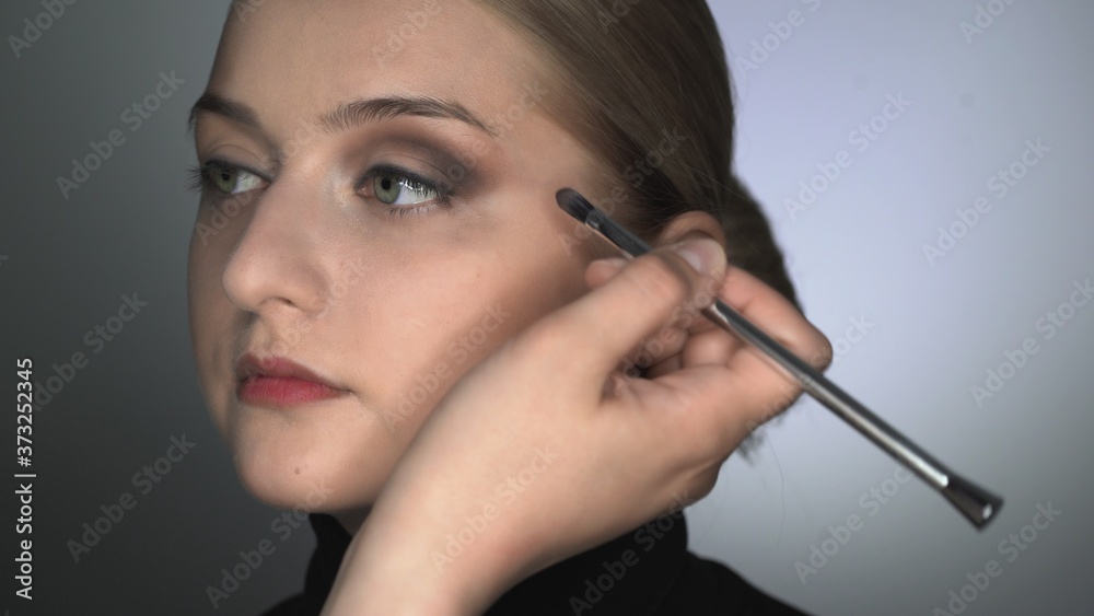 Makeup artist making professional make-up for young woman in beauty studio. Make up Artist uses brush to applies shadow on eyelid