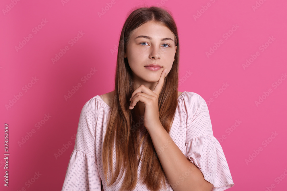 Caucasian female with long hair dressed casually looks at camera with dreamily expression, has serious expression of face, keeping index finger on cheek. Caucasian female with long hair dressed casually looks at camera with dreamily expression, has serious expression of face, keeping index finger on cheek.