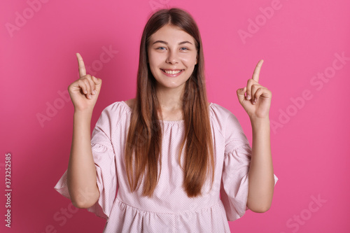 Happy smiling female wearing elegant dress looking smiling directly at camera and pointing up with fore fingers  looks happy  expressing positive emotions.
