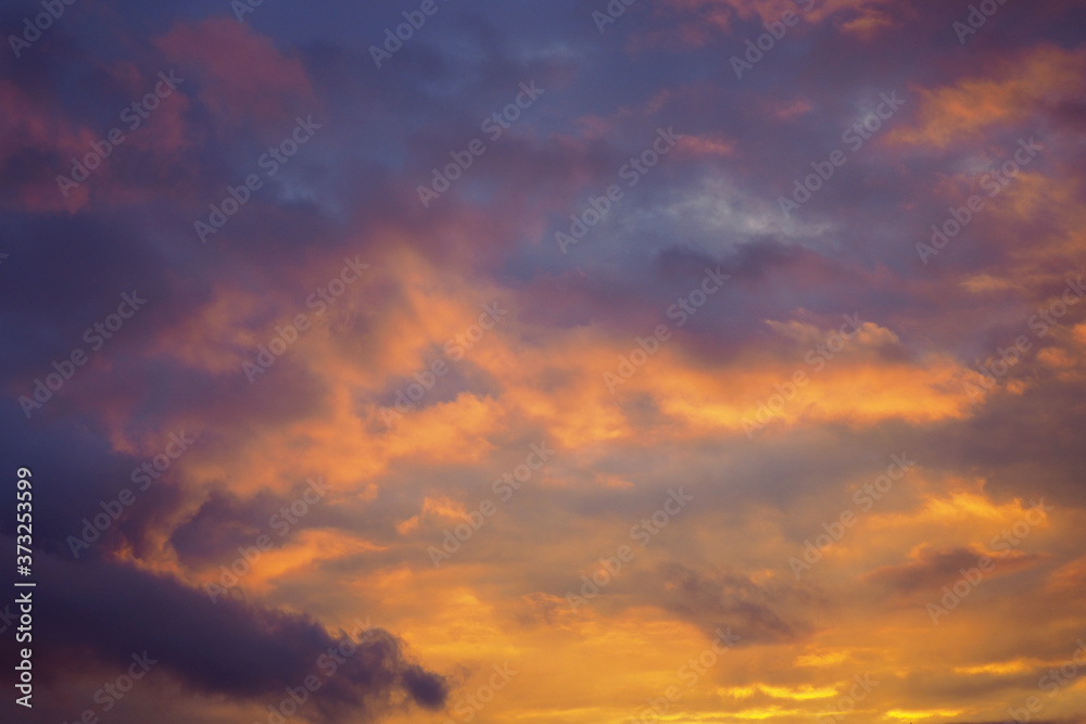 Cloudy sky at sunset. Dark violet-yellow natural background or wallpaper. The rays of the setting sun effectively illuminate the clouds. Beautiful and dramatic evening skies
