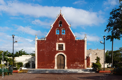 Front of the red colonial church Itzimna in a park with trees, Merida, Yucatan, Mexico photo