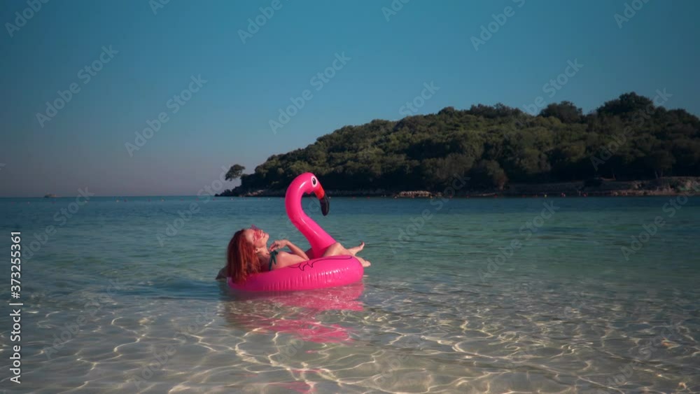 Happy woman tourist swims on an inflatable pink flamingo in the sea. Sunny day. Happy woman tourist swims on an inflatable pink flamingo in the sea. Sunny day.