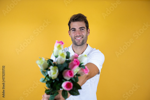 Konstfotografi young handsome man standing over yellow insolated background smiling holding flo