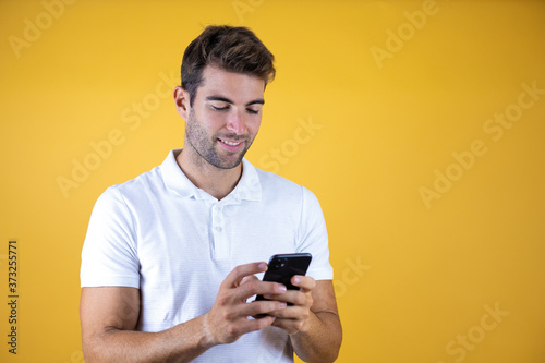 Young man having a conversation using smartphone over yellow background with a happy face standing and smiling with a confident smile showing teeth © Irene