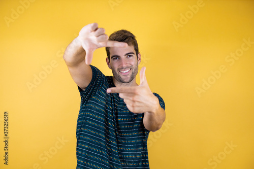 Young handsome man over yellow isolated background doing frame using hands palms and fingers, camera perspective photo