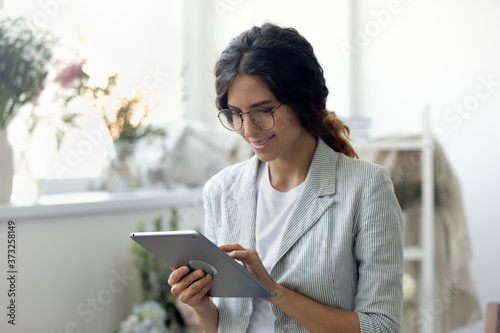 Photography Head shot smiling young beautiful businesswoman decorator clothing designer in glasses using digital computer tablet, web surfing information or consulting clients online in modern creative office