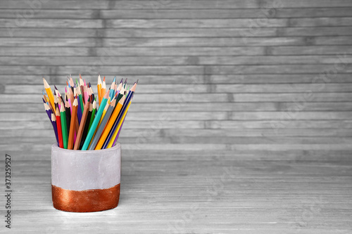 Colored pencils in a plaster cup on a natural, white background made of wooden boards. Website concept, school related topic.