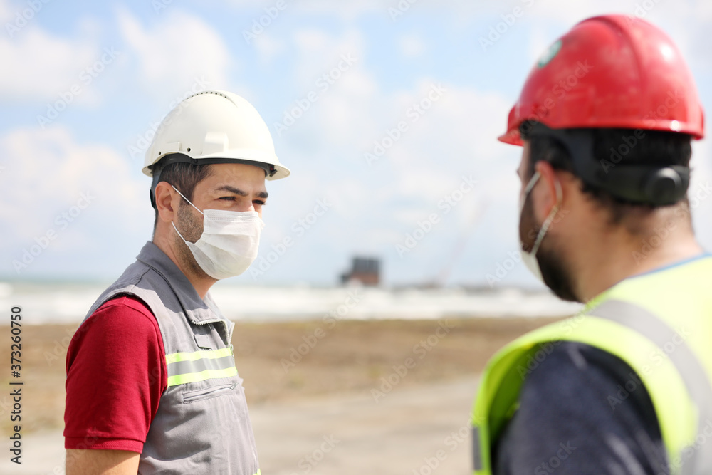Construction workers are talking about coronavirus (covid-19) with protective facemask in the construction site. Construction workers are talking about coronavirus (covid-19) with protective facemask in the construction site.