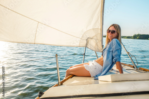 Young happy woman enjoying sunset from deck of sailing boat moving in sea at evening time. Travel, Summer, Holidays, Journey, Trip, Lifestyle, Yachting concept.