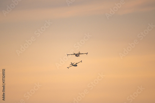 Two amphibious water bomber airplanes in flight at sunset, in France.