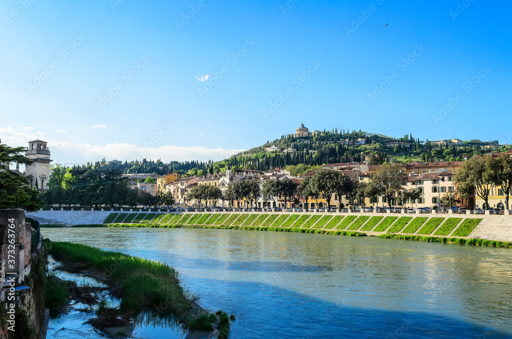 View of the embankment of Verona and the church of Santuario della Madonna di Lourdes on the top of a hill from the Ponte Pietra bridge