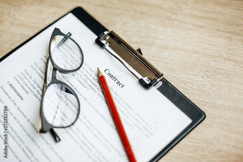 A contract on a wooden work table with glasses and a red pencil. The documents are ready for signing. Business concept. Collaboration agreement.