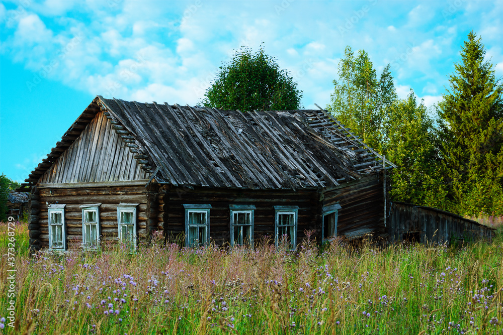 Old abandoned ruined houses among the northern forests. Abandoned crumbling village against a blue cloudy sky