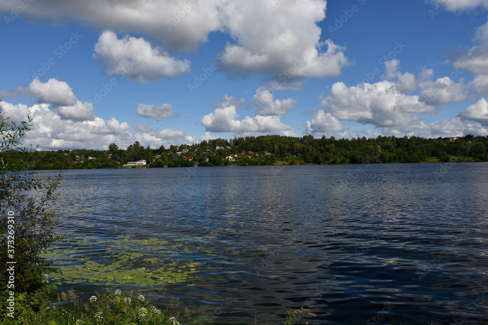 A picturesque view of a large river with green banks. Beautiful clouds are reflected in the water.