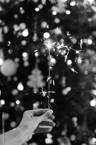 Hand holding a sparkler with a Christmas tree in black and white