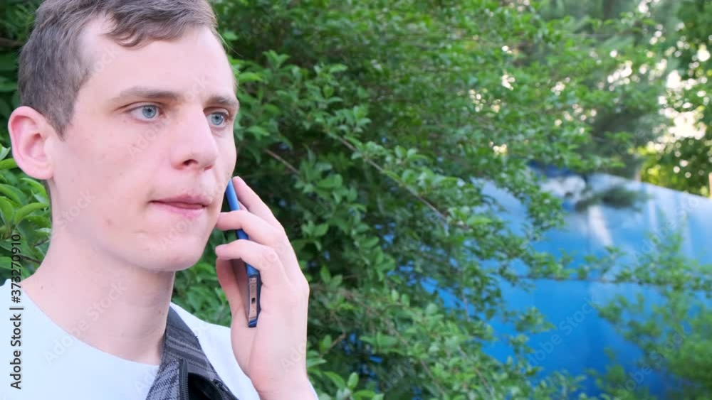 Young adult blue-eyed man drinking coffee from cardboard cup outdoors while talking on the phone