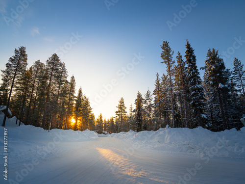 Blur image of way with snow, pine trees and blue sky with sun light. On bright and sunshine day at Kittila, Finland photo
