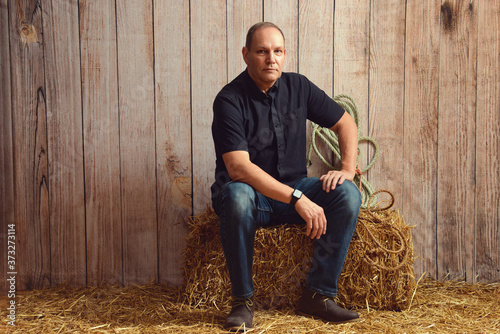 portrait of man resting on hay bale in barn photo