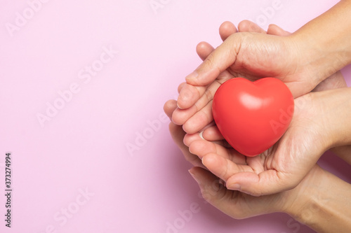 Fototapeta Naklejka Na Ścianę i Meble -  Hands holding a red heart on pink background, CSR or Corporate Social Responsibility, health care, family insurance, heart donate concept, world health day.