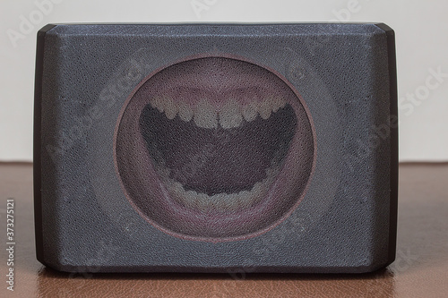 Front view of a grey loudspeaker with a screaming mouth inside on top of a leather table. Communication and game concept.