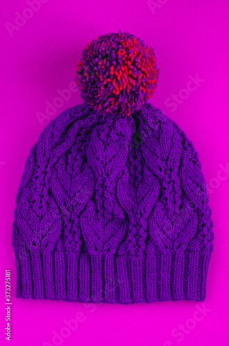 Beautiful kace handknitted hat with multicolored pompon on pink background. Top view photo